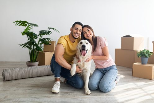 A man and a woman with a golden retriever dog and moving boxes in the background