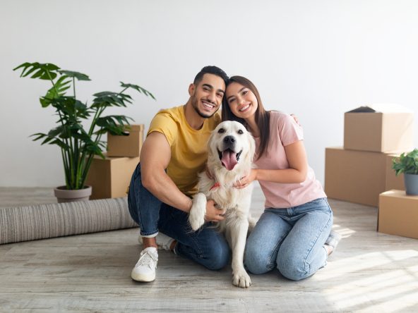 A man and a woman with a golden retriever dog and moving boxes in the background